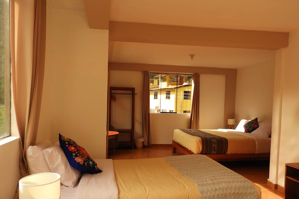 A hotel room with two beds, a window with curtains, a small table, and a lamp.