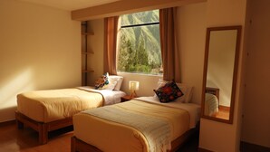 Una habitación con dos camas, un ventanal con cortinas, un espejo y suelo de madera.