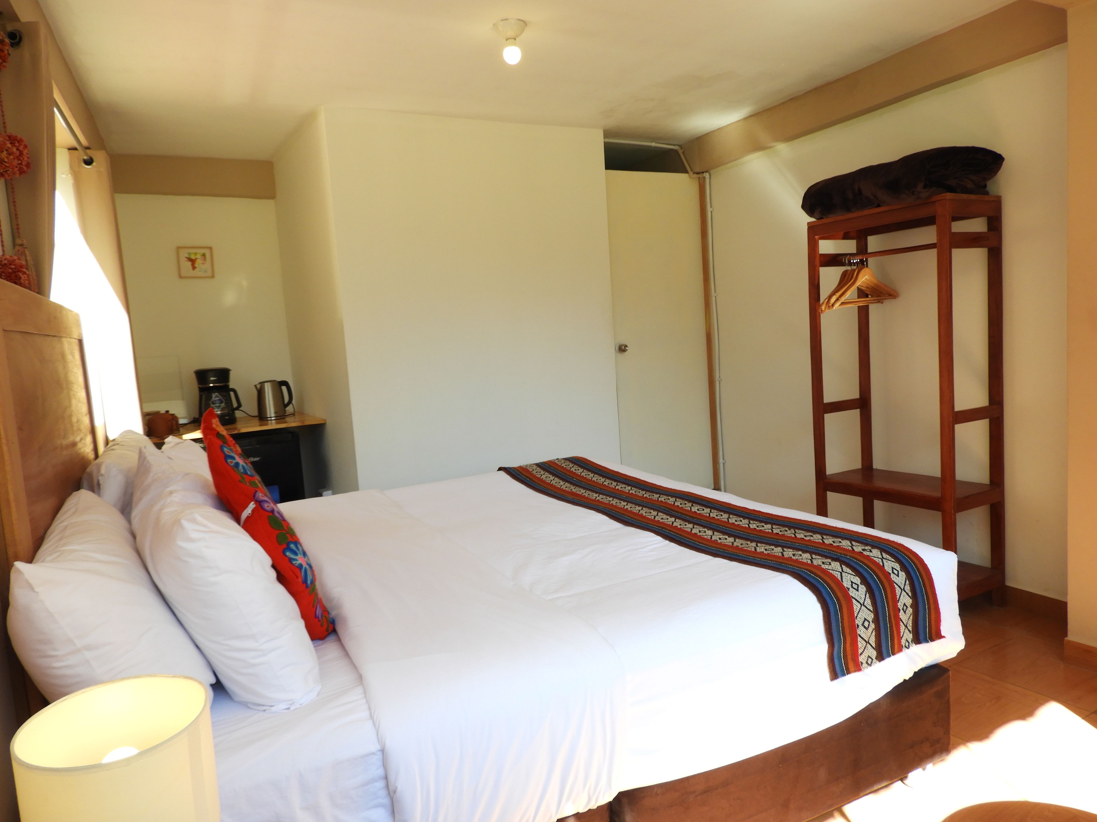 A hotel room with a bed, a desk with a coffee maker, and a wooden shelf.