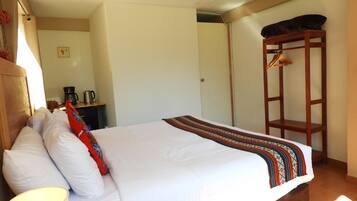 A hotel room with a bed, a desk with a coffee maker, and a wooden shelf.