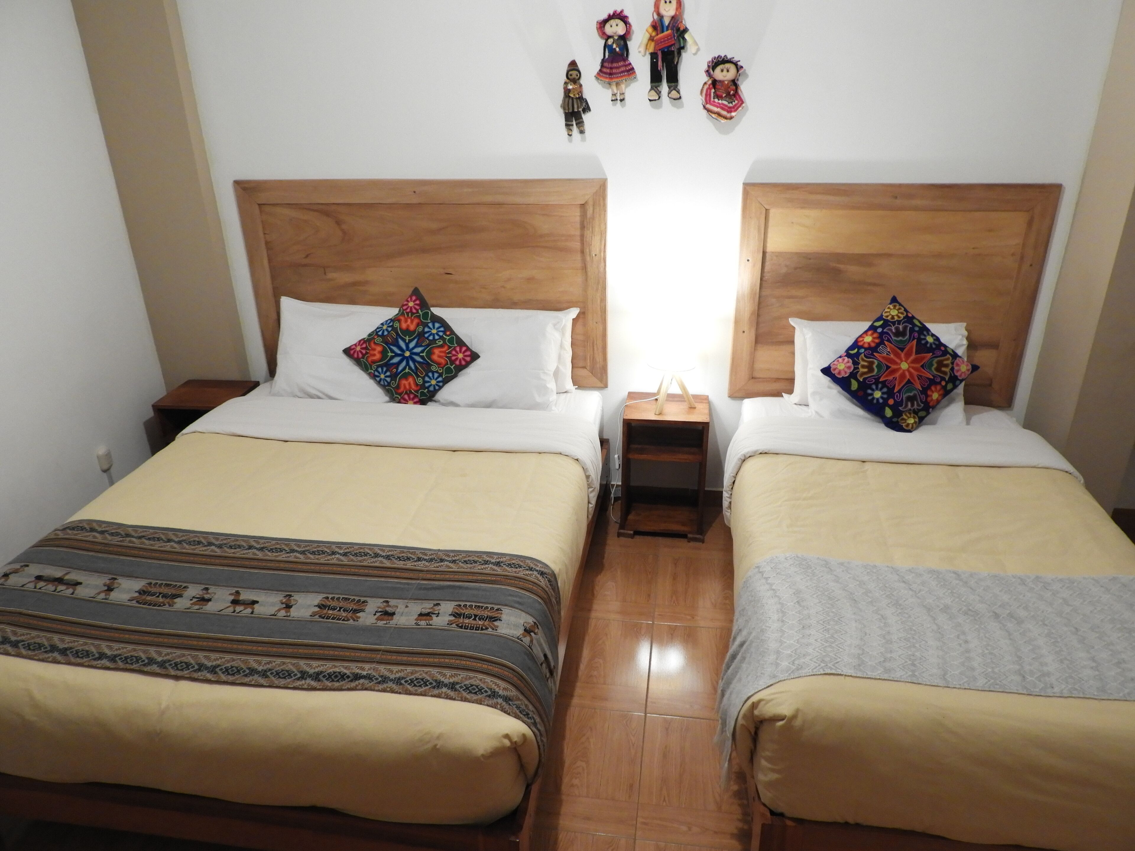 A double room with two beds, each with a wooden headboard, a bedside table, and a colorful pillow.