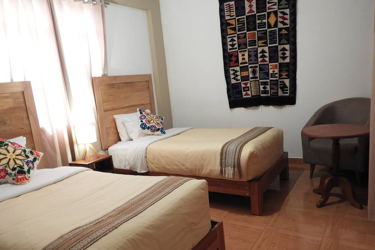 A hotel room with two beds, a wooden headboard, a small table, and a chair.