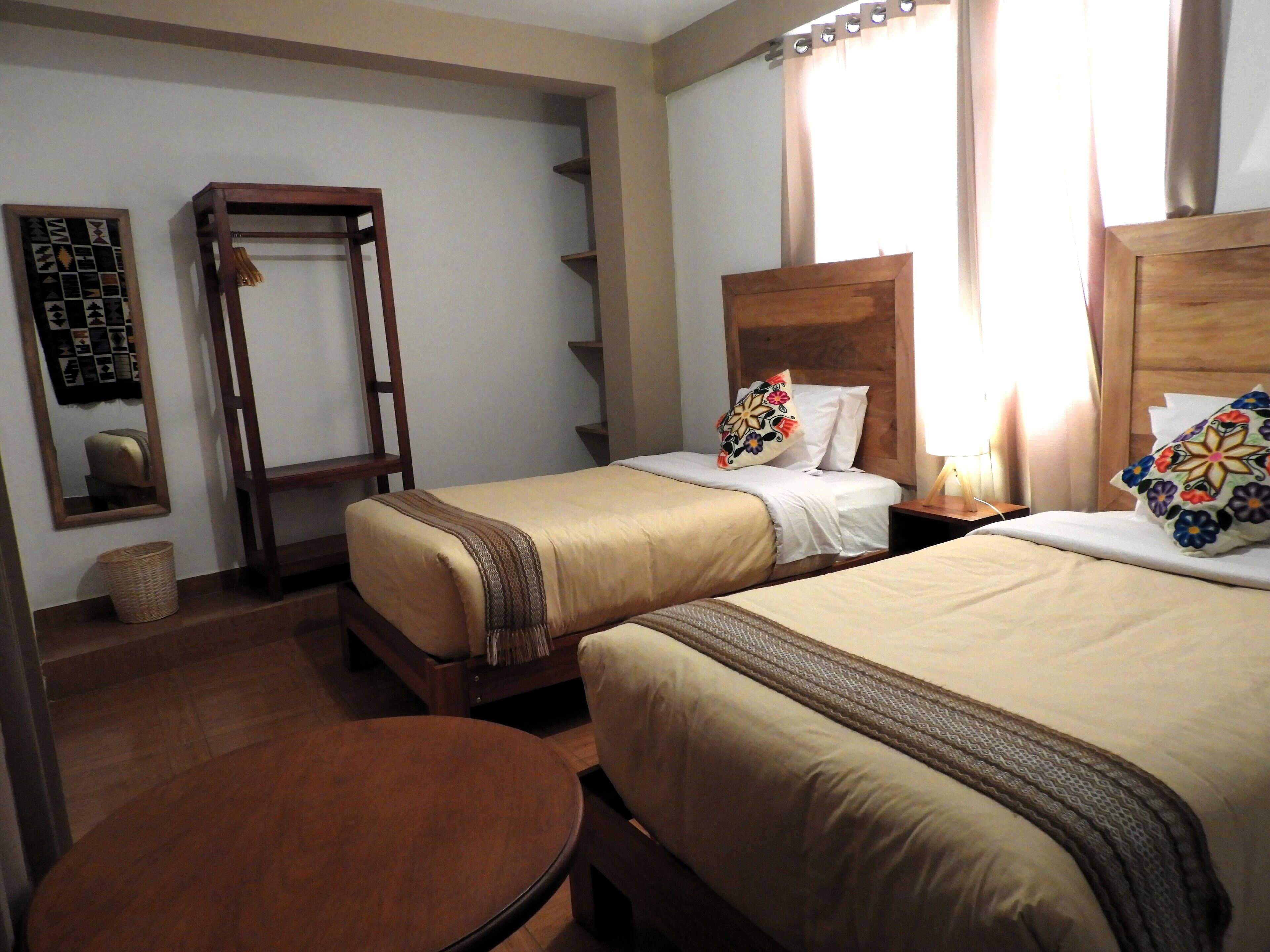 A hotel room with two beds, a wooden headboard, a small round table, and a mirror on the wall.