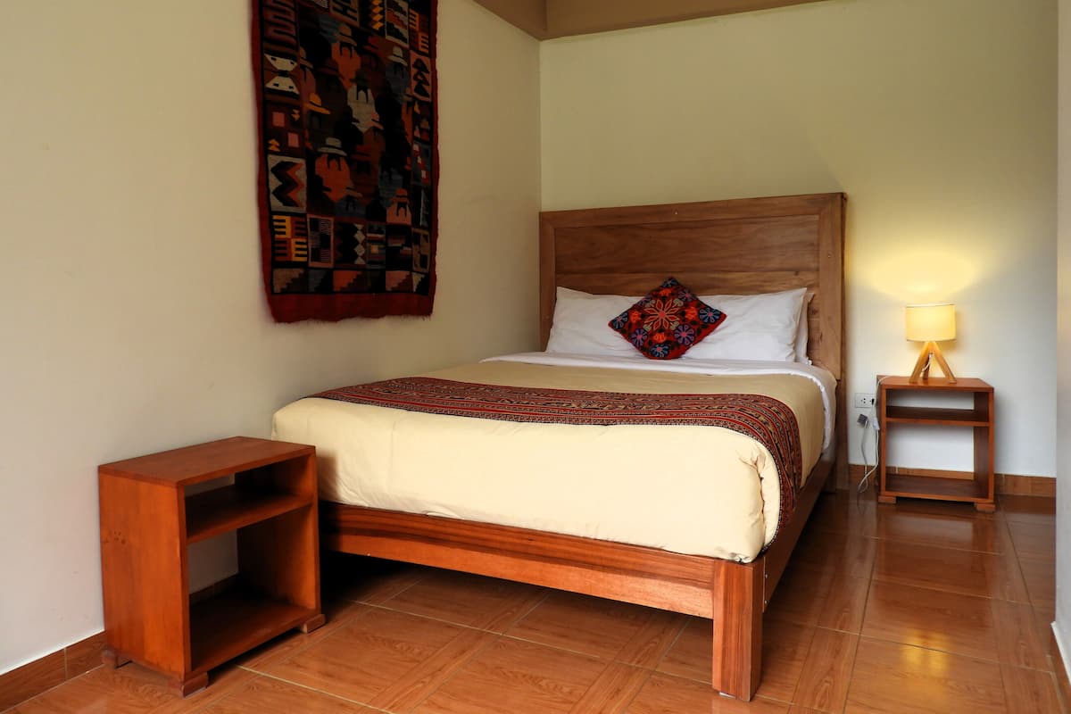 A neatly arranged bedroom with a wooden bed, a bedside table, a nightstand, and a wall hanging.