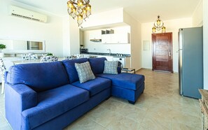 A modern living room with a blue sectional sofa, a dining area, a kitchen, and a wooden door. - Full Seaview beautiful apartment (Red Sea Governorate)