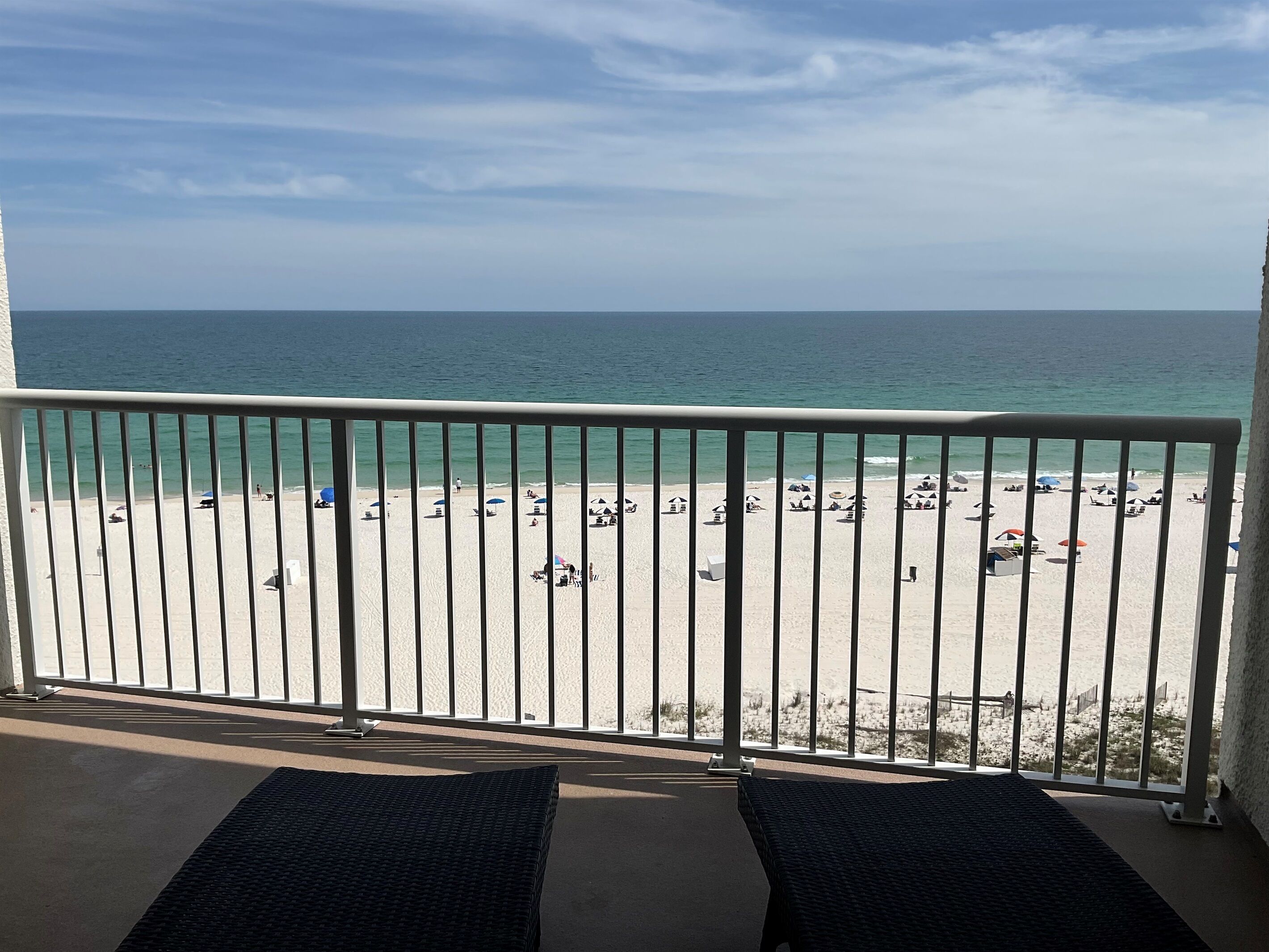 A balcony with a view of a beach, white railings, and two wicker chairs.