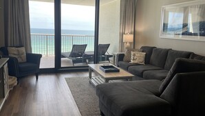 Un salon comprenant un canapé, un fauteuil et une table basse. Il y a un balcon avec vue sur la mer.
