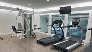 Une salle de sport équipée de tapis de course, d’appareils de musculation et d’un écran de télévision.