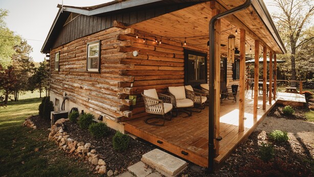 A log cabin with a wooden deck, wicker chairs, and a covered porch. - Fire Pit, 10 private Acres | Pets Welcome (Bourbon)