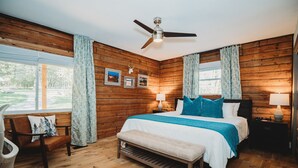 A wooden-paneled bedroom with a bed, bench, chair, and two bedside tables with lamps. - Fire Pit, 10 private Acres | Pets Welcome (Bourbon)