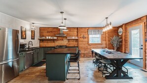 A modern kitchen with wooden walls, stainless steel appliances, and a central island with bar stools. - Fire Pit, 10 private Acres | Pets Welcome (Bourbon)