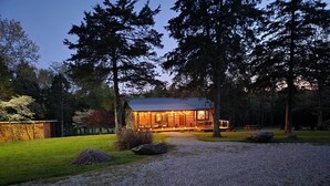 A log cabin with a porch and a gravel driveway, surrounded by trees. - Fire Pit, 10 private Acres | Pets Welcome (Bourbon)