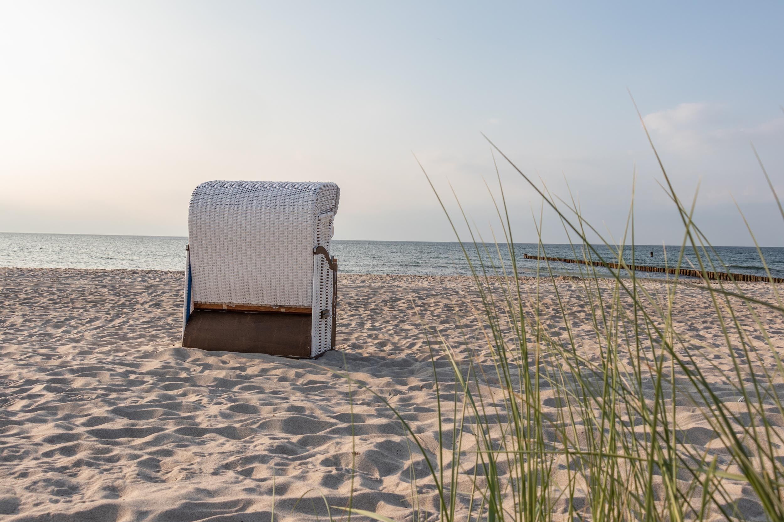 Ein Liegestuhl am sandigen Strand, im Hintergrund das Meer.