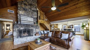 Un salon chaleureux avec une cheminée en pierre, un canapé en cuir, une table basse en bois et un escalier menant à un étage supérieur.