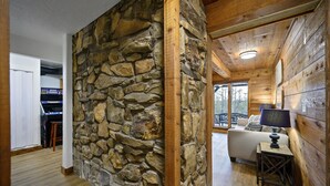 L’intérieur d’une cabane en rondins, avec un mur en pierre, un plafond en bois et un coin salon confortable agrémenté d’une lampe.