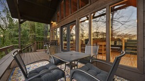 Un espace extérieur abrité, doté d’une table et de chaises, de grandes fenêtres et offrant une vue sur les arbres environnants.