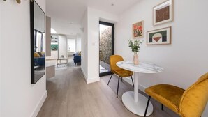 A modern interior with a round table and two chairs, a large mirror, and artwork on the wall. - Cozy London House with Garden & Terrace | Near Westfield Stratford & Tube (London)