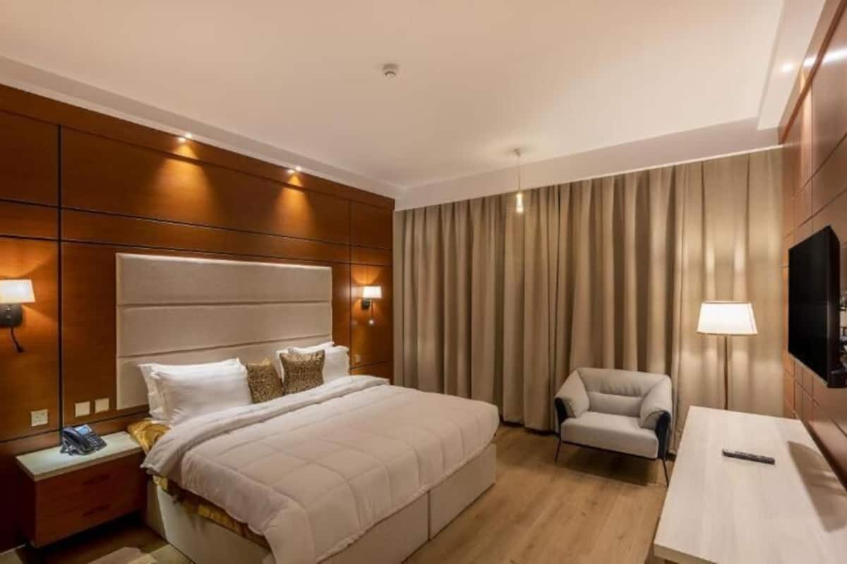 Une chambre d’hôtel avec un grand lit, une table de chevet, une chaise, un téléviseur et un téléviseur fixé au mur.