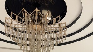 Ein modernes Interieur mit einer großen Chandelieber, zwei Sesseln, einem runden Tisch und einer Lampe vor einer gestreiften Wand.