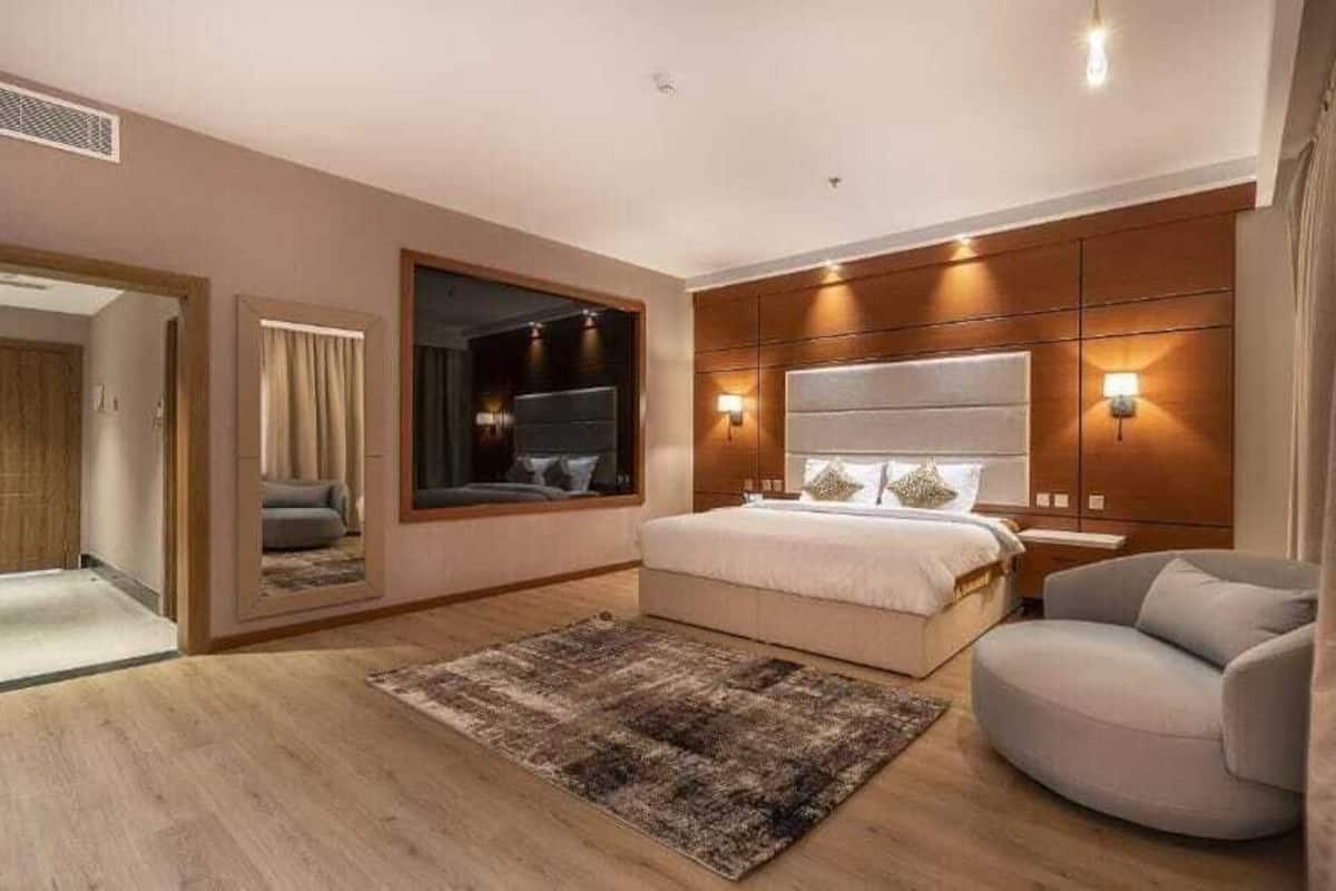 Une chambre à coucher avec un grand lit, un coin salon avec un fauteuil, un miroir et un luminaire fixé au mur.