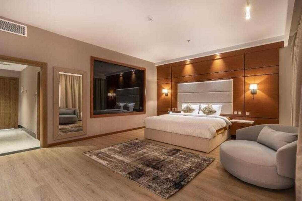 Une chambre à coucher avec un grand lit, un coin salon avec un fauteuil, un miroir et un luminaire fixé au mur.