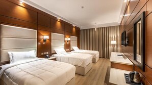 Une chambre d’hôtel avec trois lits, un bureau, une chaise, une télévision et un mini-bar.