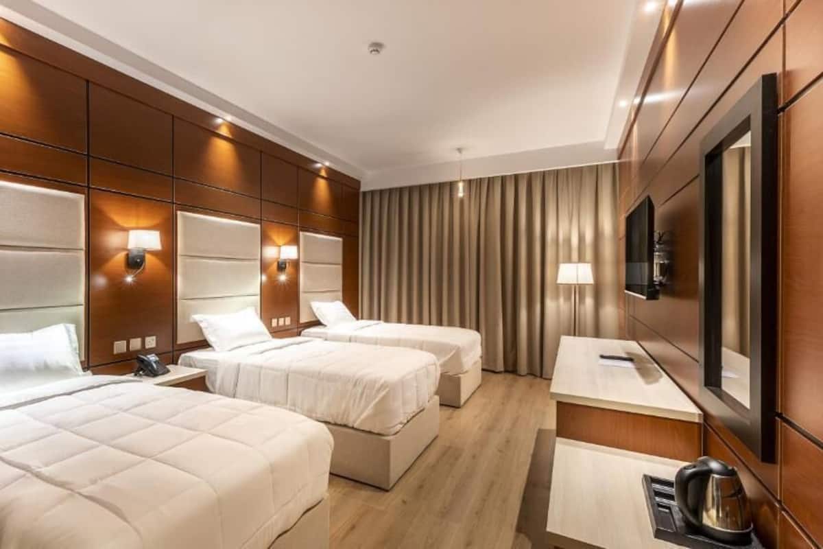 Une chambre d’hôtel avec trois lits, un bureau, une chaise, une télévision et un mini-bar.