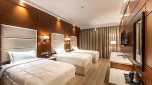 A hotel room with three beds, a desk, a chair, a TV, and a minibar. - Flavor Hotel (Madinah)