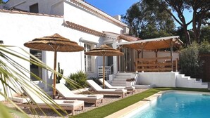 A poolside area with lounge chairs and umbrellas, a pool, and a white building with a tiled roof.