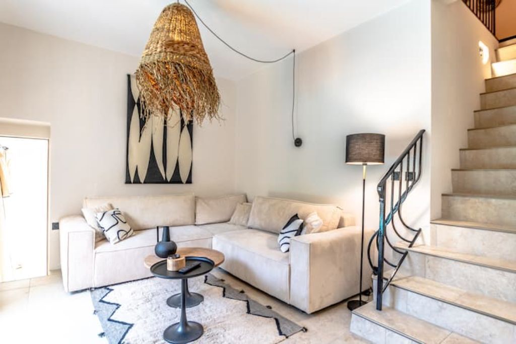 Un salon moderne avec un canapé d’angle, une table basse ronde et un luminaire original orné de plumes.