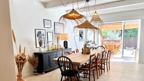 A spacious dining area with a long wooden table and chairs, a black cabinet, and hanging wicker lamps.