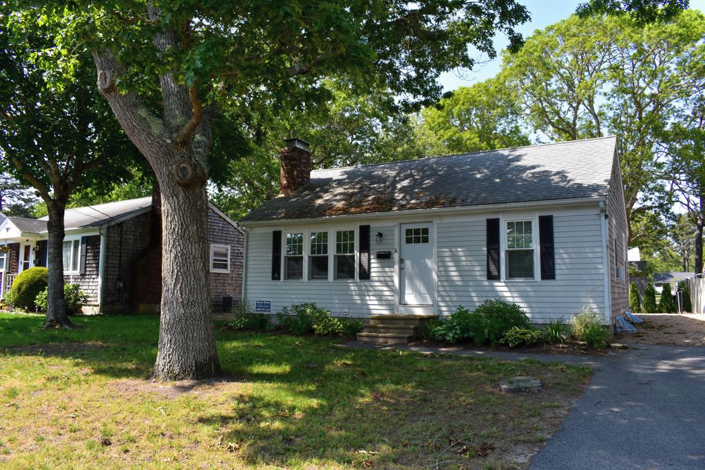 A single-story house with a front porch, a chimney, and a large tree in front.