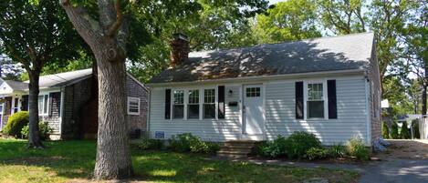 A single-story house with a front porch, a chimney, and a large tree in front.