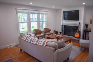 Un salon comprenant un canapé, deux fauteuils, une table basse, une cheminée et un téléviseur fixé au mur.