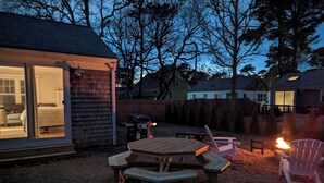 Un jardin avec une table et des chaises en bois, un foyer et un barbecue.