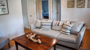 Un salon avec un canapé gris, des coussins à rayures, une table basse en bois et une fresque représentant des poissons, encadrée, sur le mur.
