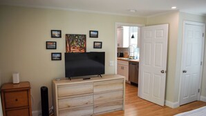 Une chambre à coucher avec un téléviseur posé sur une commode en bois, un lit et une porte donnant sur une salle de bain.