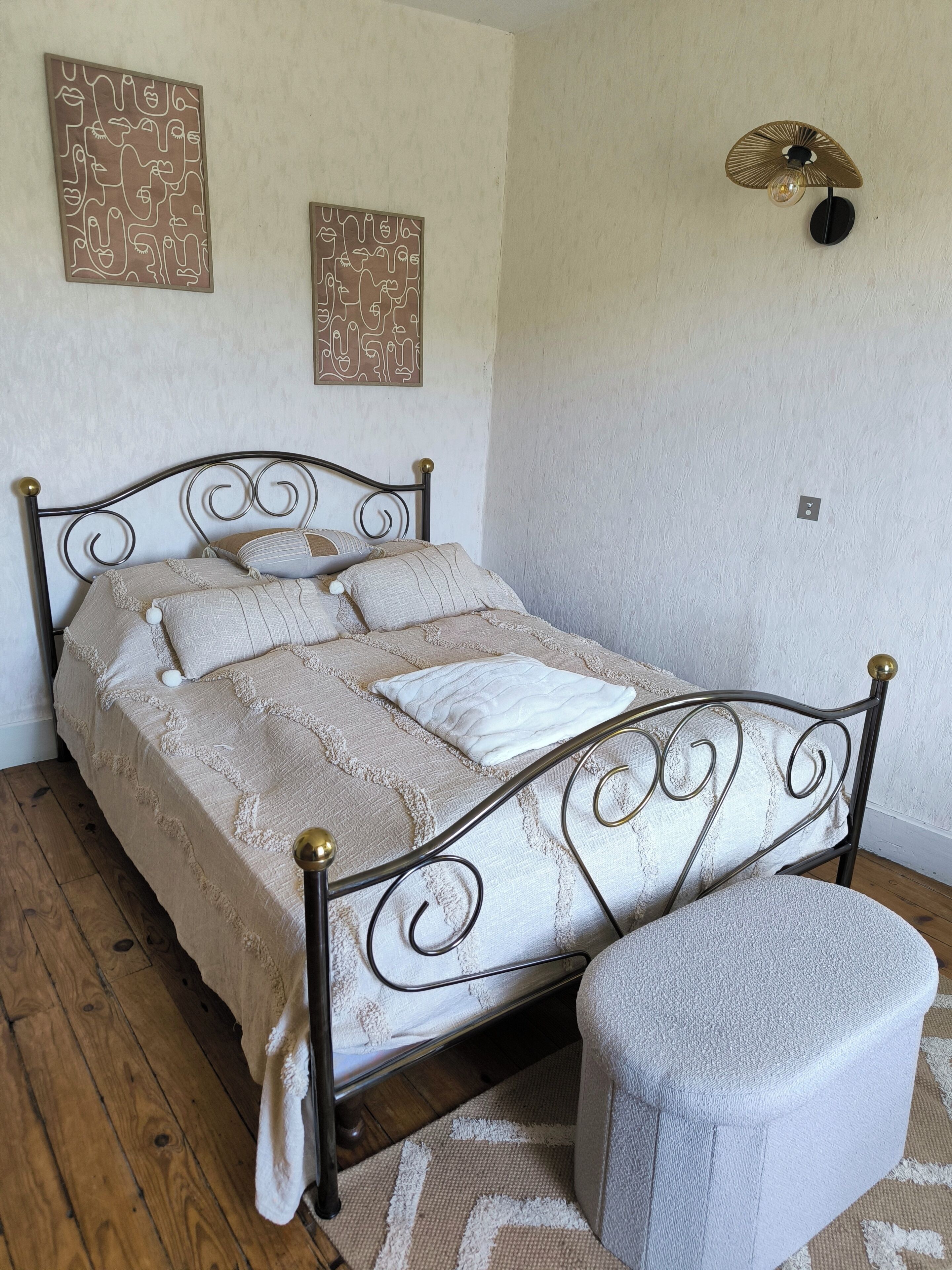 Una cama bien tendida con estructura metálica, una mesita de noche y dos lámparas fijadas a la pared.