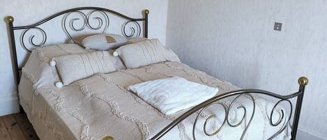 Una cama bien tendida con estructura metálica, una mesita de noche y dos lámparas fijadas a la pared.