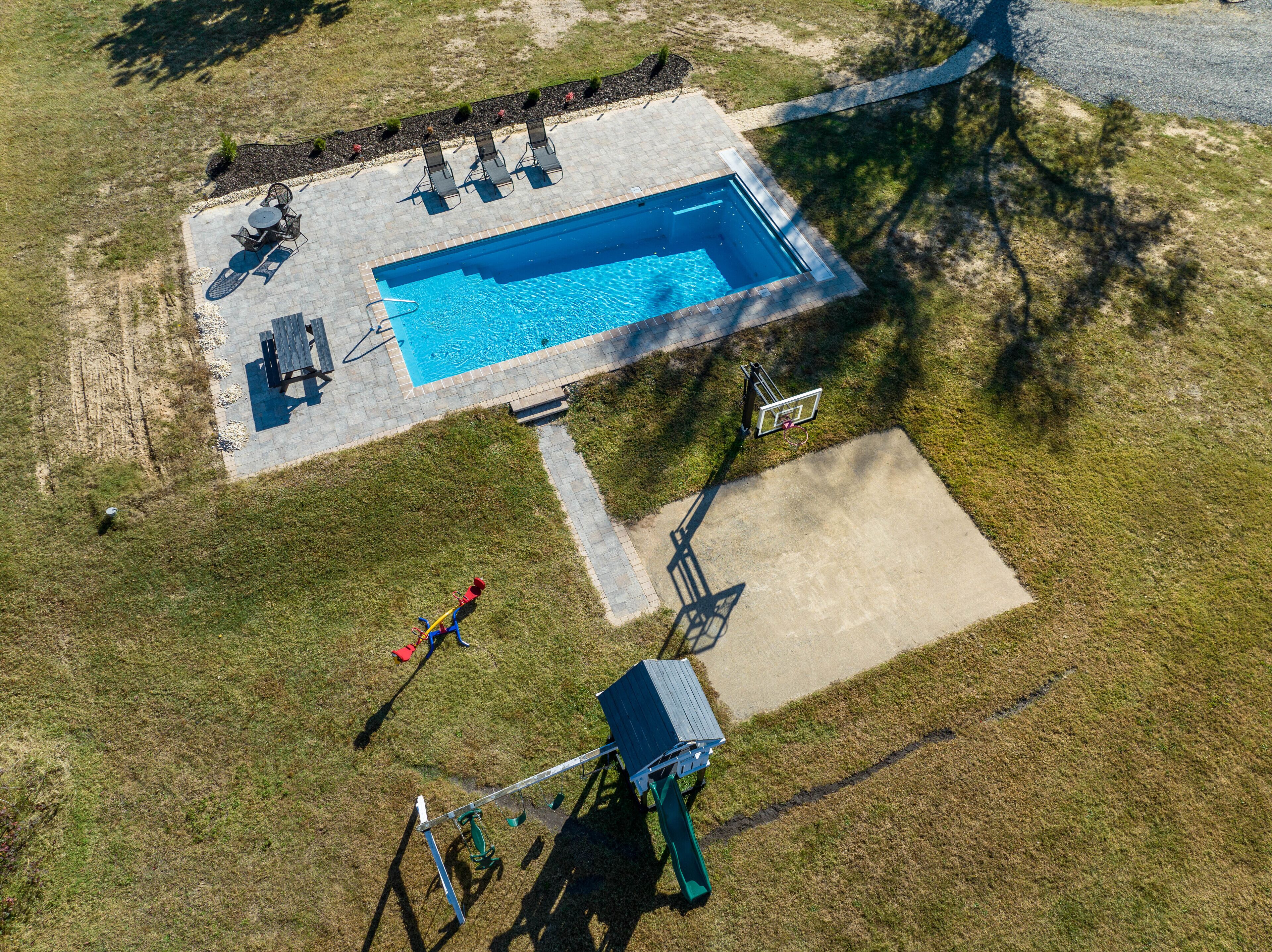 An aerial view of a swimming pool area with a basketball court, lounge chairs, and a slide.