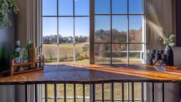 A wooden bar counter with a view of a field and trees through large windows. - Tranquil Lakefront Farm Oasis ~ Pool ~ Scenic View<br>  (Bumpass)