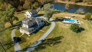 A large house with a swimming pool, a covered porch, and a small dock by a lake. - Tranquil Lakefront Farm Oasis ~ Pool ~ Scenic View<br>  (Bumpass)