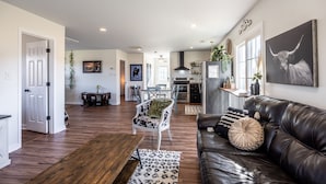 A spacious living area with a leather sofa, a dining table, and a kitchen in the background. - Tranquil Lakefront Farm Oasis ~ Pool ~ Scenic View<br>  (Bumpass)