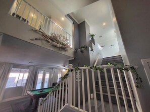 Staircase connects two levels, featuring a pool table on the lower floor.