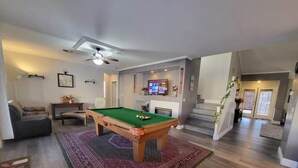 Ein Wohnzimmer mit Billardtisch, einer Couch, einem Fernseher und einer Treppe.