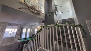 Ein mehrgeschossiges Interieur mit Billardtisch, Treppen und dekorativen Pflanzen.