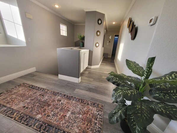 Enter a stylish hallway leading to a well-equipped kitchen area with a potted plant and decorative art.