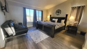 Ein Schlafzimmer mit Bett, einer Couch, einem Schreibtisch, einer Lampe und einem Fenster mit Vorhängen.