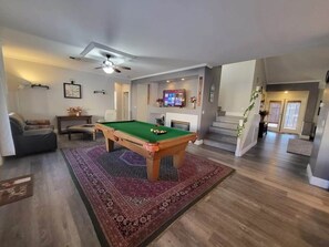 Relax in this inviting living area with a pool table, television, and staircase leading to an upper level.