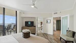 A hotel room with a large bed, a TV, a balcony with a view of the city, and a dining area. - Beachfront at Destin Harbor's East Pass! Epic Views, Pool, Private Beach! (Destin)